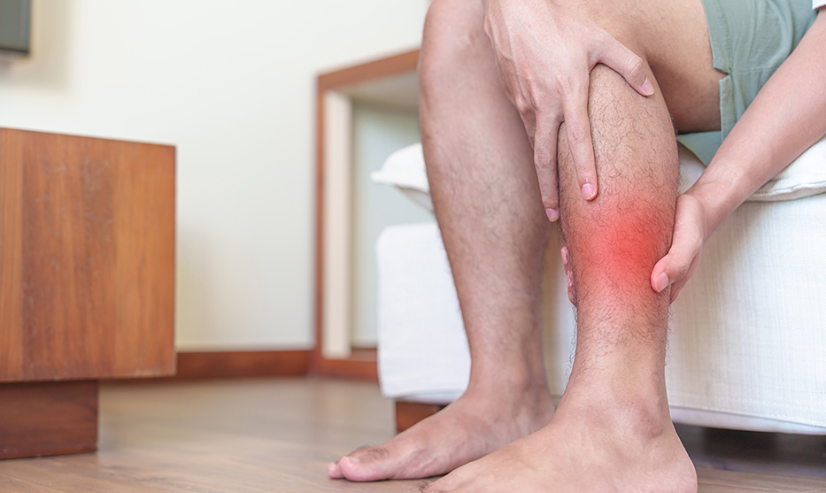 A close-up of a person sitting down and clutching their painful calf muscle, which is highlighted with a red sore spot graphic.